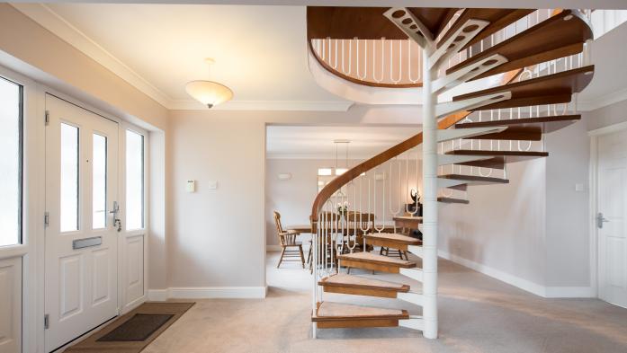 A general interior view of a retro style spiral staircase made of wood and metal in a open-plan hallway dining room with grey walls and beige carpet