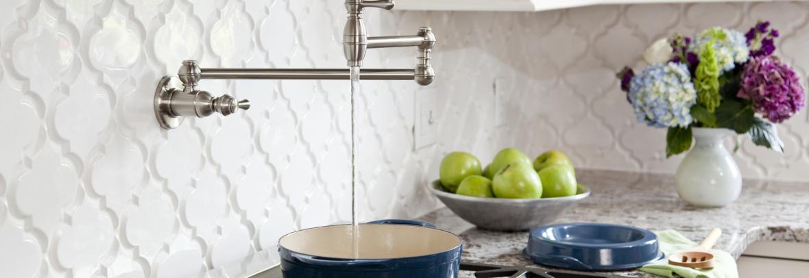 A pot filler faucet above a gas stove pours water into a cooking pot