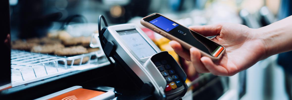 Hand holding a cell phone over a payment reader