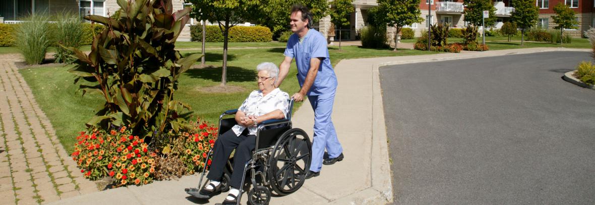 Nurse pushes an older woman in a wheelchair in front of a senior living home