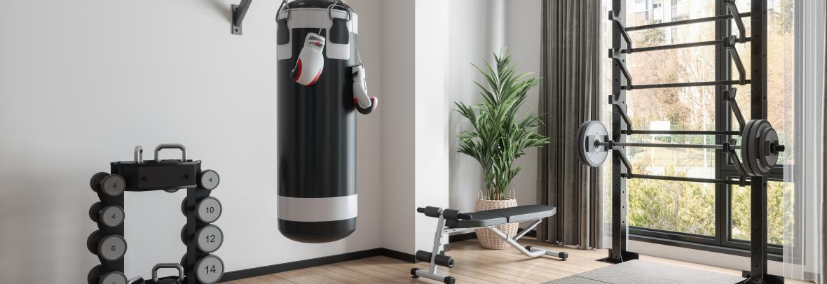 Home Gym With Barbell, Dumbbells, Boxing Bag And Other Sports Equipments in a large room with a big windows and wood floors.