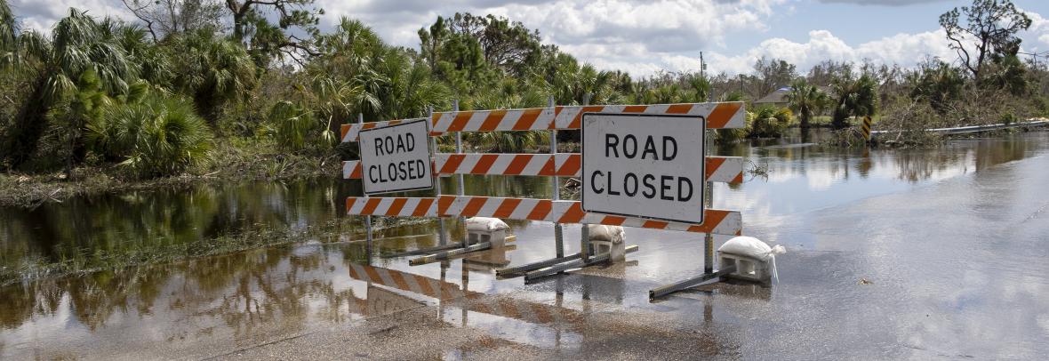 Flooded street in Florida after hurricane rainfall with road closed signs blocking driving of cars. Safety of transportation during natural disaster concept.