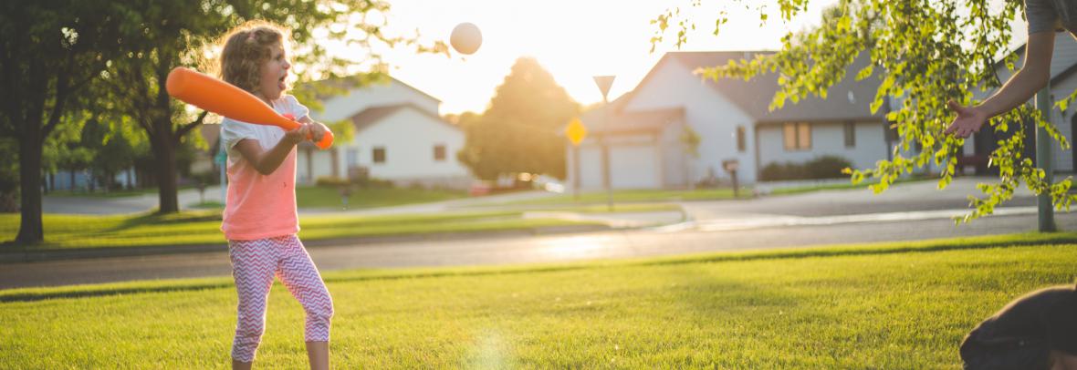 girl playing baseball with mom in yard