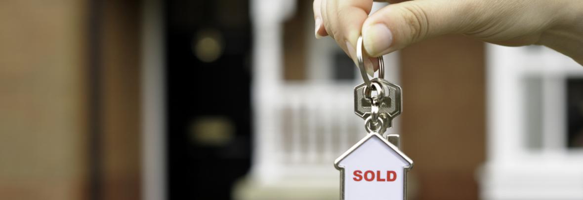 Hand in front of a house holding keychain with "sold" inside small house