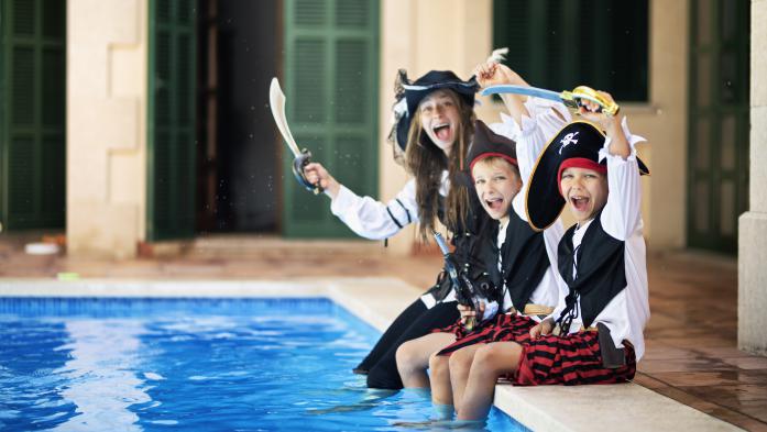 Three kids dresses as pirates dip their feet in a swimming pool