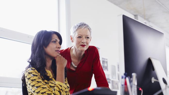 Mature woman mentoring younger woman at computer in business setting