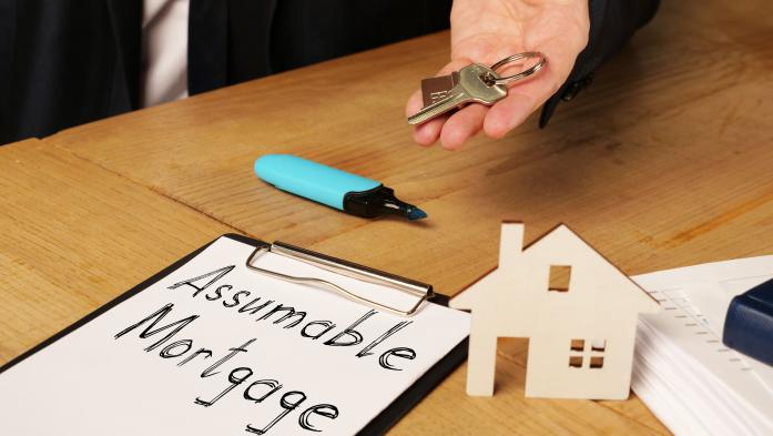 Assumable mortgage written on a clipboard and a man's hand holding the keys to a house