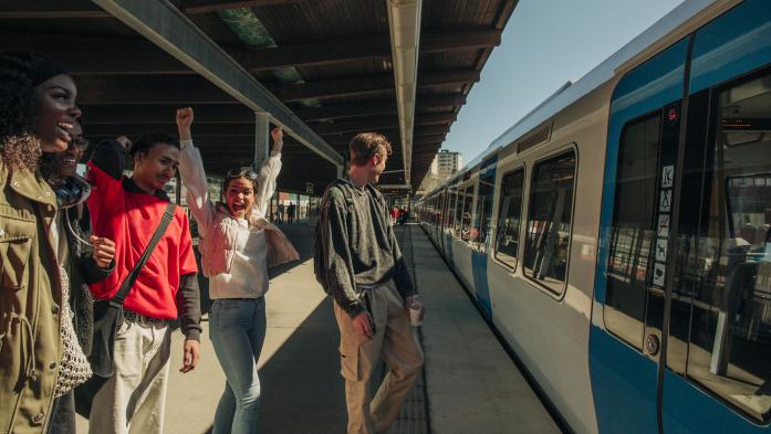 Four people cheer the arrival of a train in a local train station