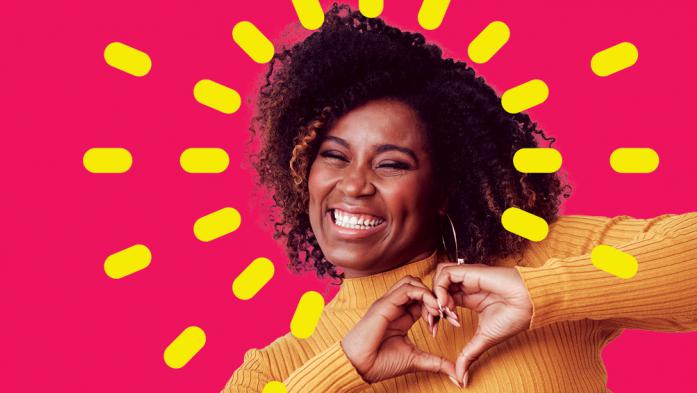 African American woman making a heart shape with hands on magenta background