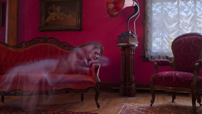 Woman's ghost lies on a red couch in a red old-fashioned room