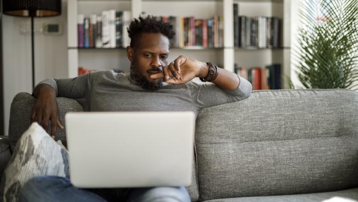 man who appears concerned looking at laptop while sitting on couch