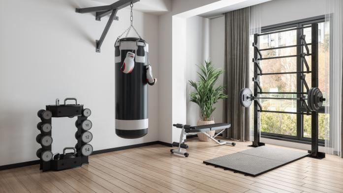 Home Gym With Barbell, Dumbbells, Boxing Bag And Other Sports Equipments in a large room with a big windows and wood floors.