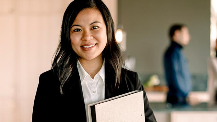 Photo of an asian, female real estate agent with clients in the background
