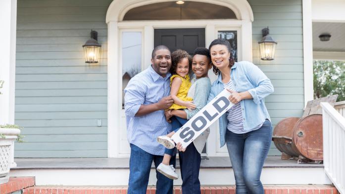family on front porch of house holding sold sign