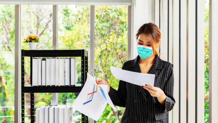 Woman wearing mask in office looking at paperwork