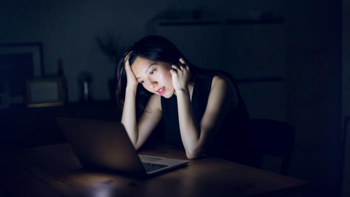 woman in dark on phone looking at laptop