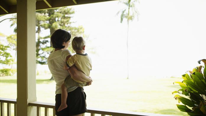 Mother holding toddler son on porch looking out
