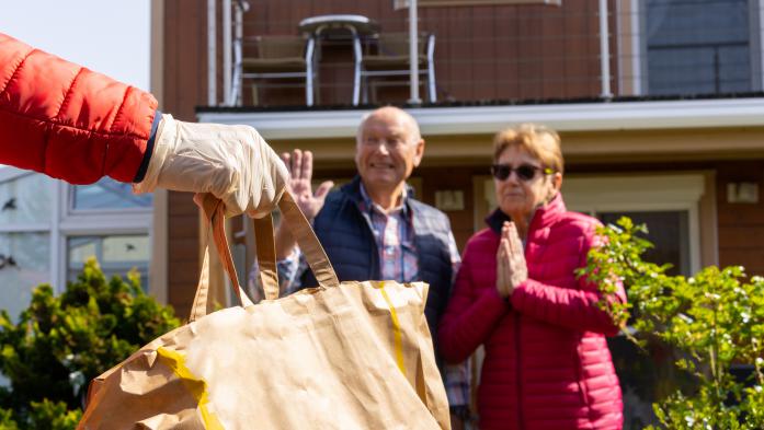 Gloved hand holding grocery bag delivered to thankful older couple 