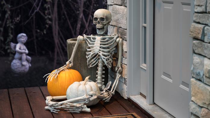 Skeleton and Halloween decorations on front porch by welcome mat