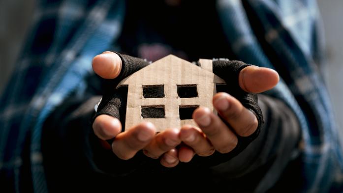 Homeless man holds cardboard cutout of a house