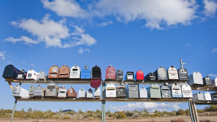 Row of country mailboxes in different colors against a deep blue sky with clouds