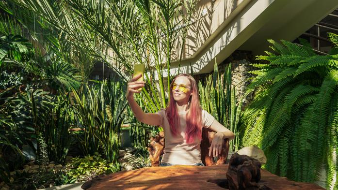 A woman taking a selfie photo amid an inside garden with trees and plants